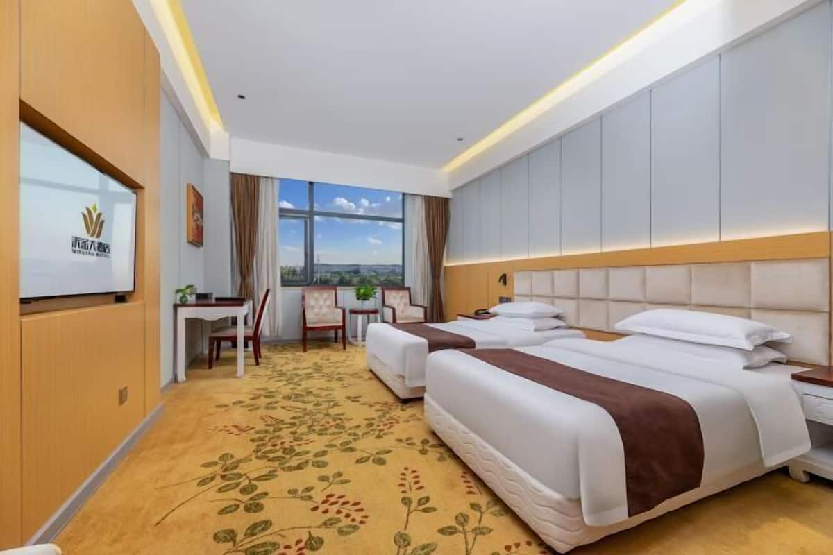 A hotel room with two beds, a desk, a chair, and a large window.