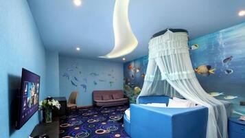 A room with a bed, a TV, a sofa, and a wall mural of fish.