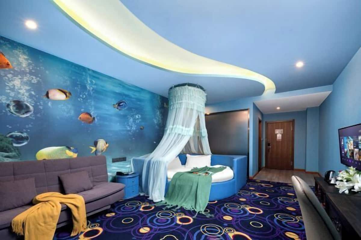 A room with a blue wall mural of fish, a bed with a canopy, a sofa, and a patterned carpet.
