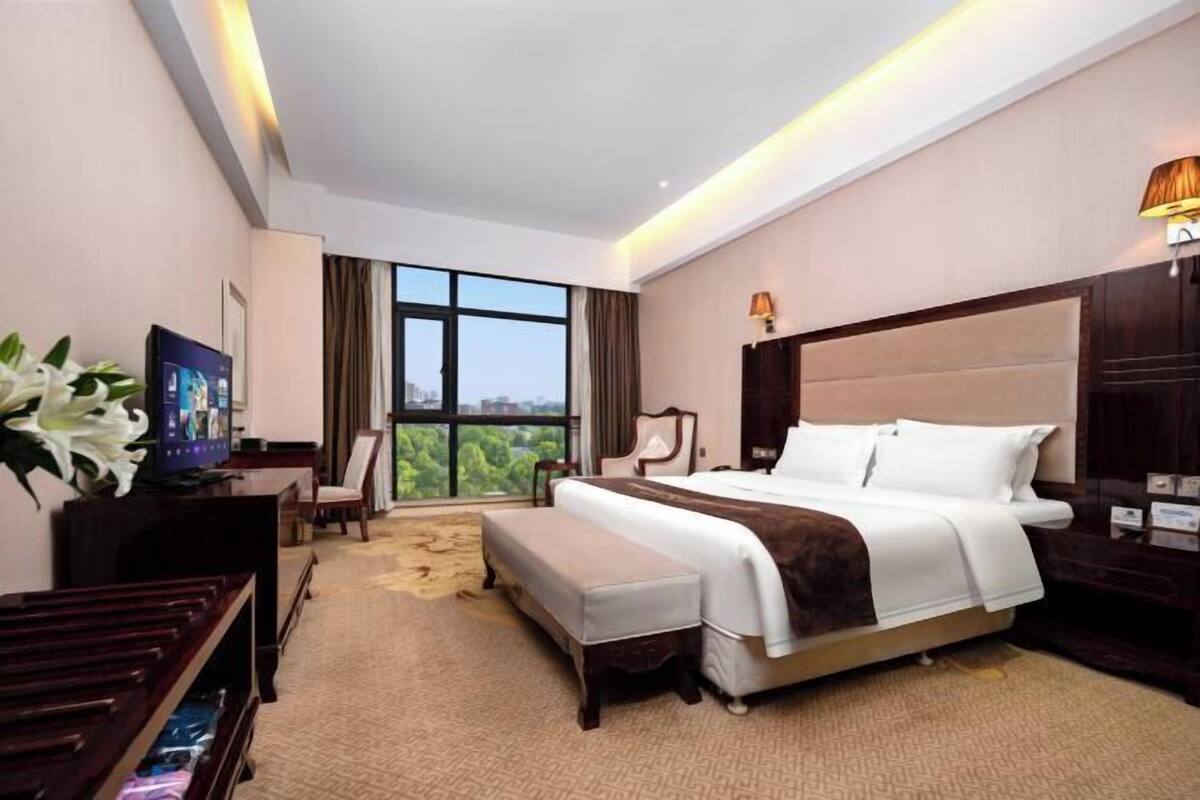A hotel room with a large bed, a desk, a television, and a view of the outdoors.