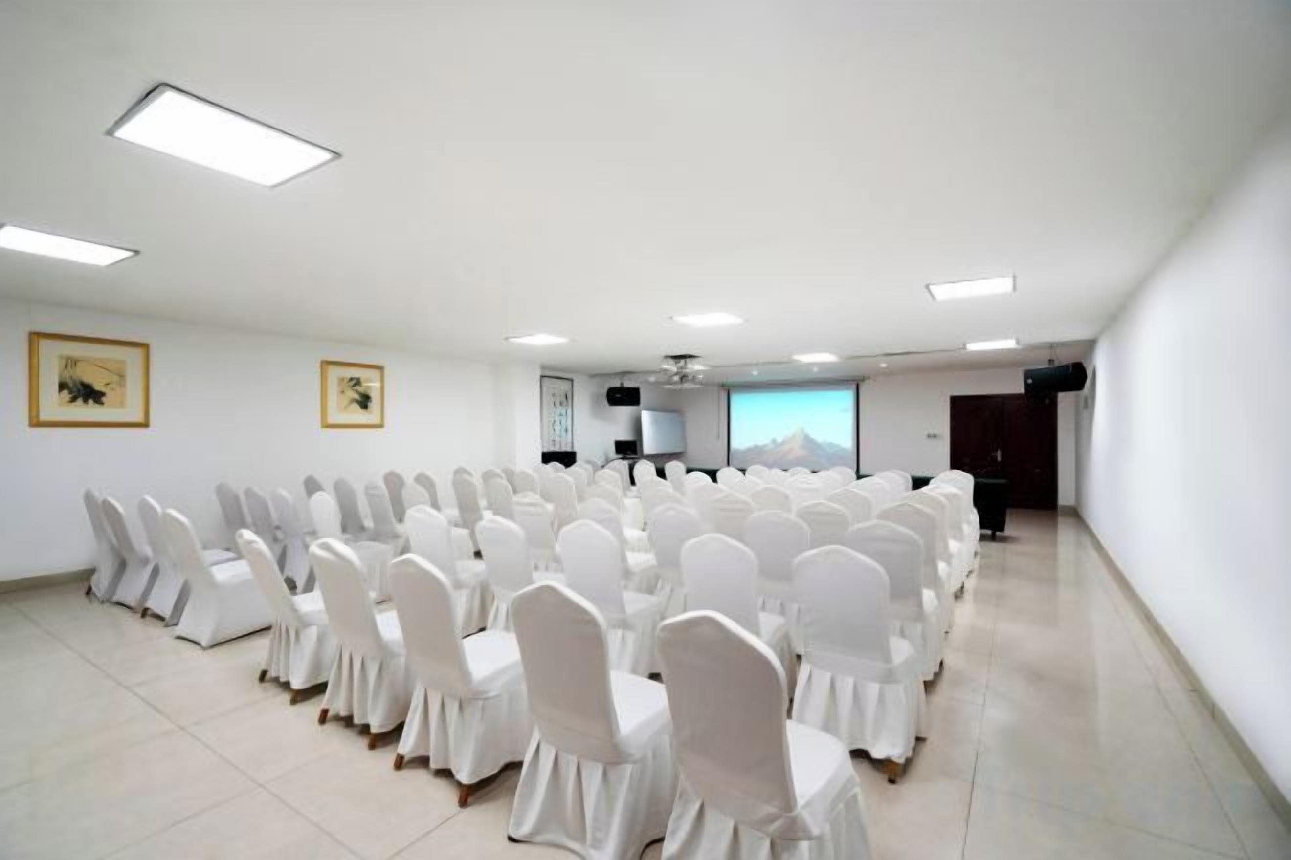A conference room with rows of white chairs, a projector screen, and a large window with a mountain view.
