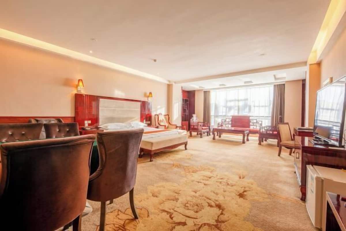 A hotel room with a large bed, a desk with a television, and a seating area with chairs and a table.