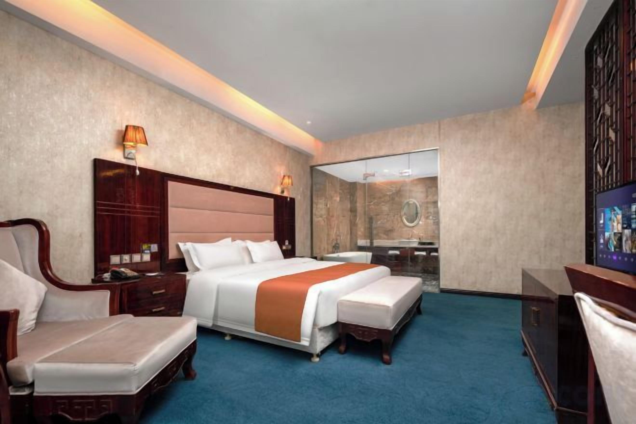 A hotel room with a large bed, a sitting area, a desk, and a mirror.