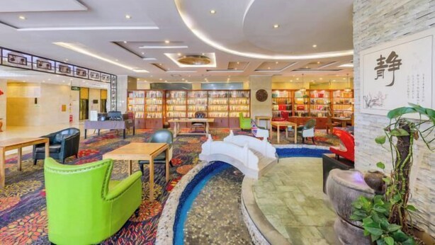 Un espacio interior moderno con una fuente central, zonas de estar y estanterías llenas de libros.