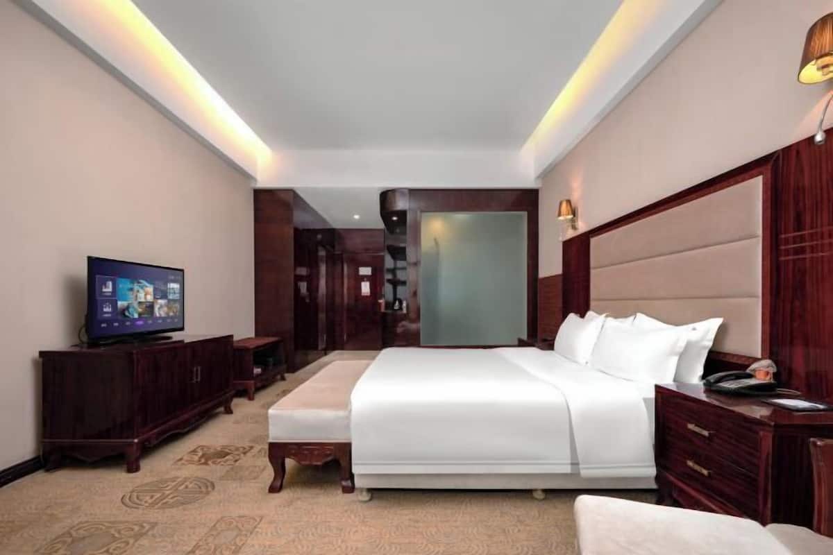 A hotel room with a large bed, a television, a wooden cabinet, and a mirror.