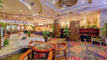 A hotel lobby with a carpeted floor, seating area with chairs and tables, and a bookshelf.