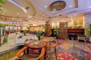 A hotel lobby with a carpeted floor, seating area with chairs and tables, and a bookshelf. - Wojin Hotel (Zhengzhou Xinzheng International Airport) (Zhongmu)