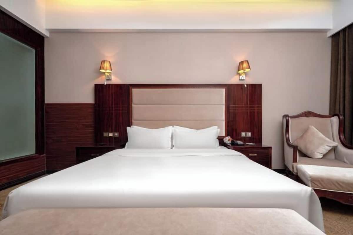 A hotel room with a large bed, two bedside tables, a chair, and two wall-mounted lamps.