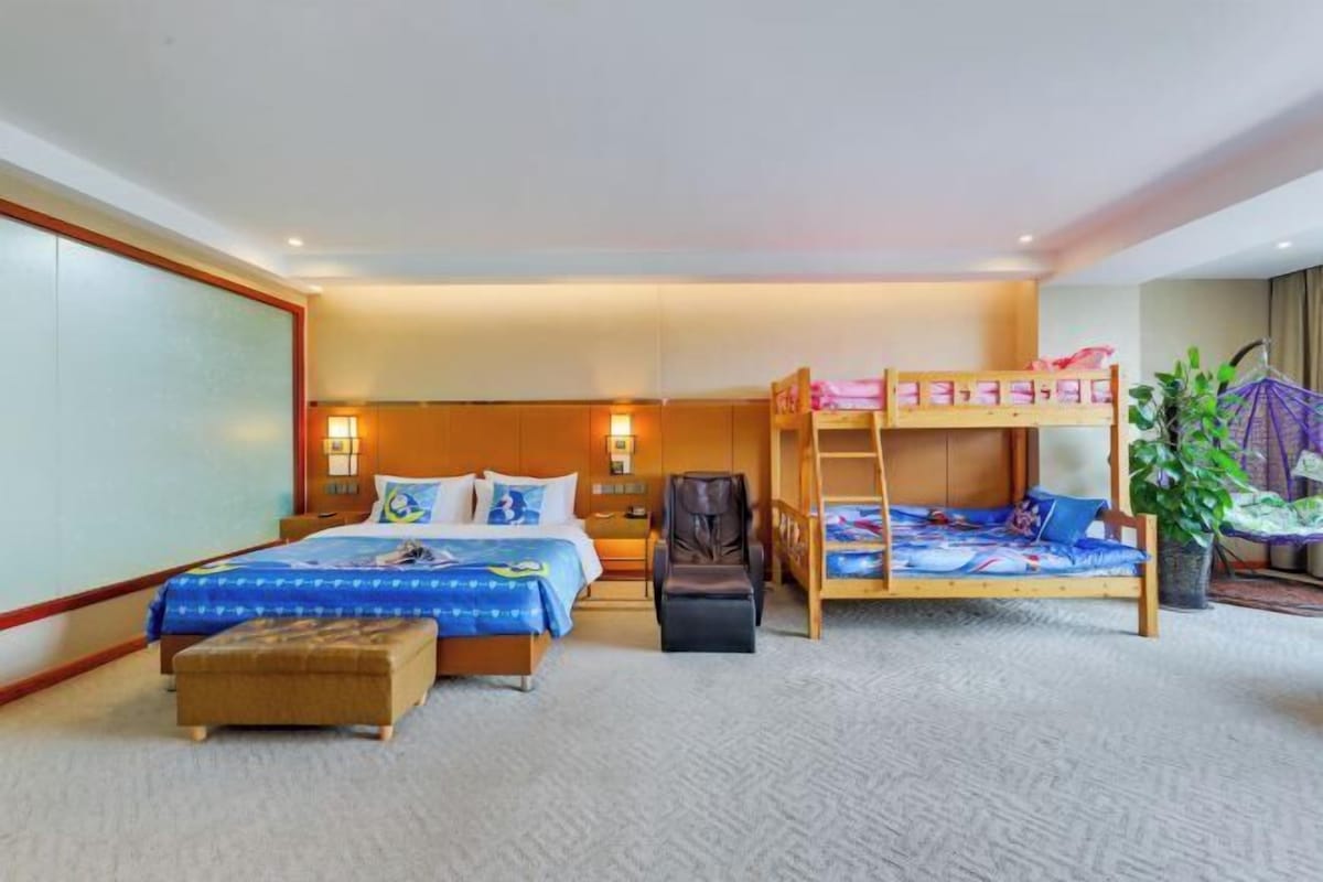 Een hotelkamer met een stapelbed, een enkel bed, een massagestoel en een potplant.