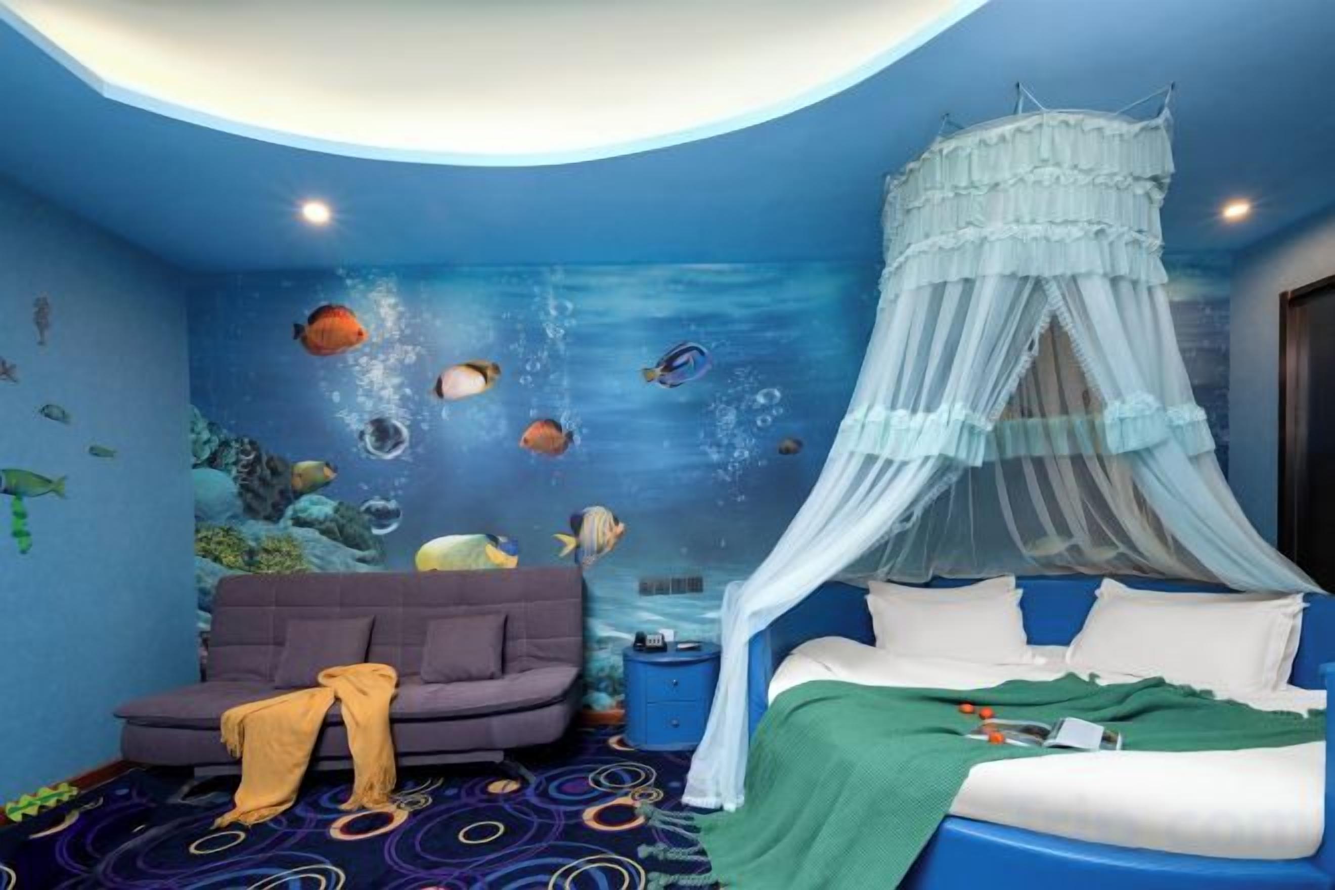 A bedroom with a bed under a canopy, a sofa, and a wall mural of an underwater scene.