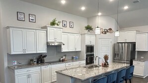 A modern kitchen with white cabinets, a large island with bar stools, stainless steel appliances, and pendant lighting.