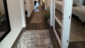 A hallway with a wooden floor, a rug, and a sliding barn door leading to a bedroom with a bed and a nightstand.