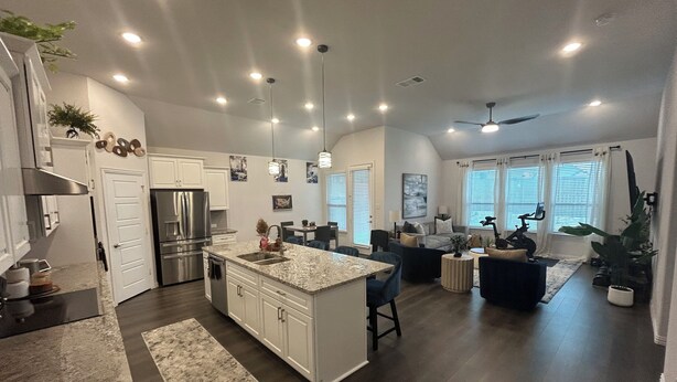 A spacious kitchen with a central island, a dining area with a table and chairs, a living room with a sofa and a coffee table, and a ceiling fan.