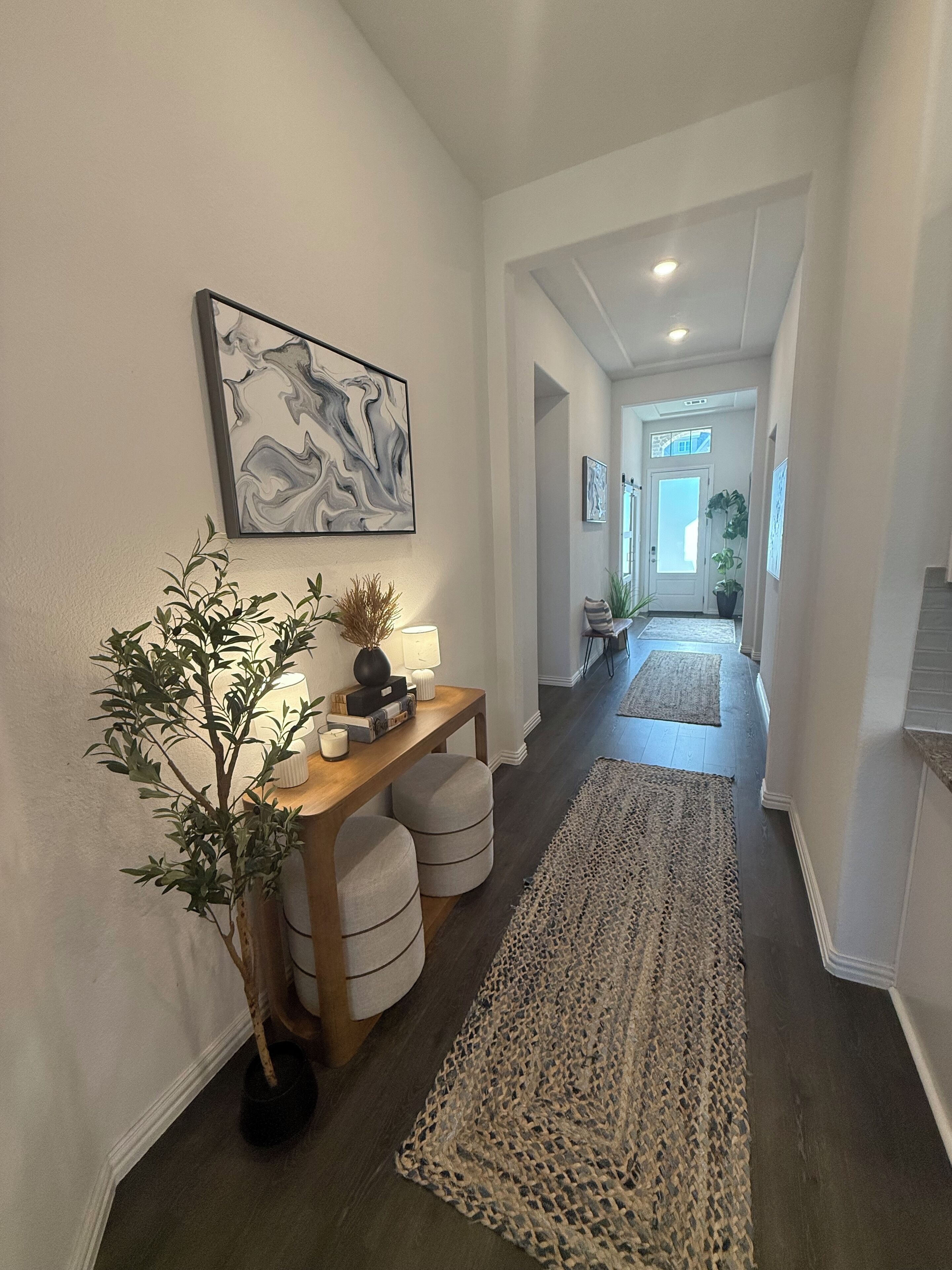 Un couloir avec une console en bois, une grande peinture abstraite, une plante en pot et un long tapis tissé.