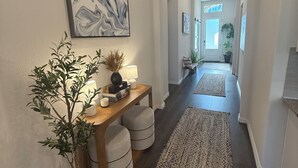 A hallway with a wooden console table, a large abstract painting, a potted plant, and a long woven rug.