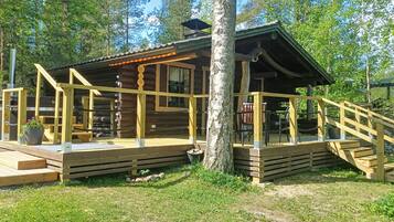 Een houten chalet met een veranda en een trap die er naartoe leidt, omringd door bomen.