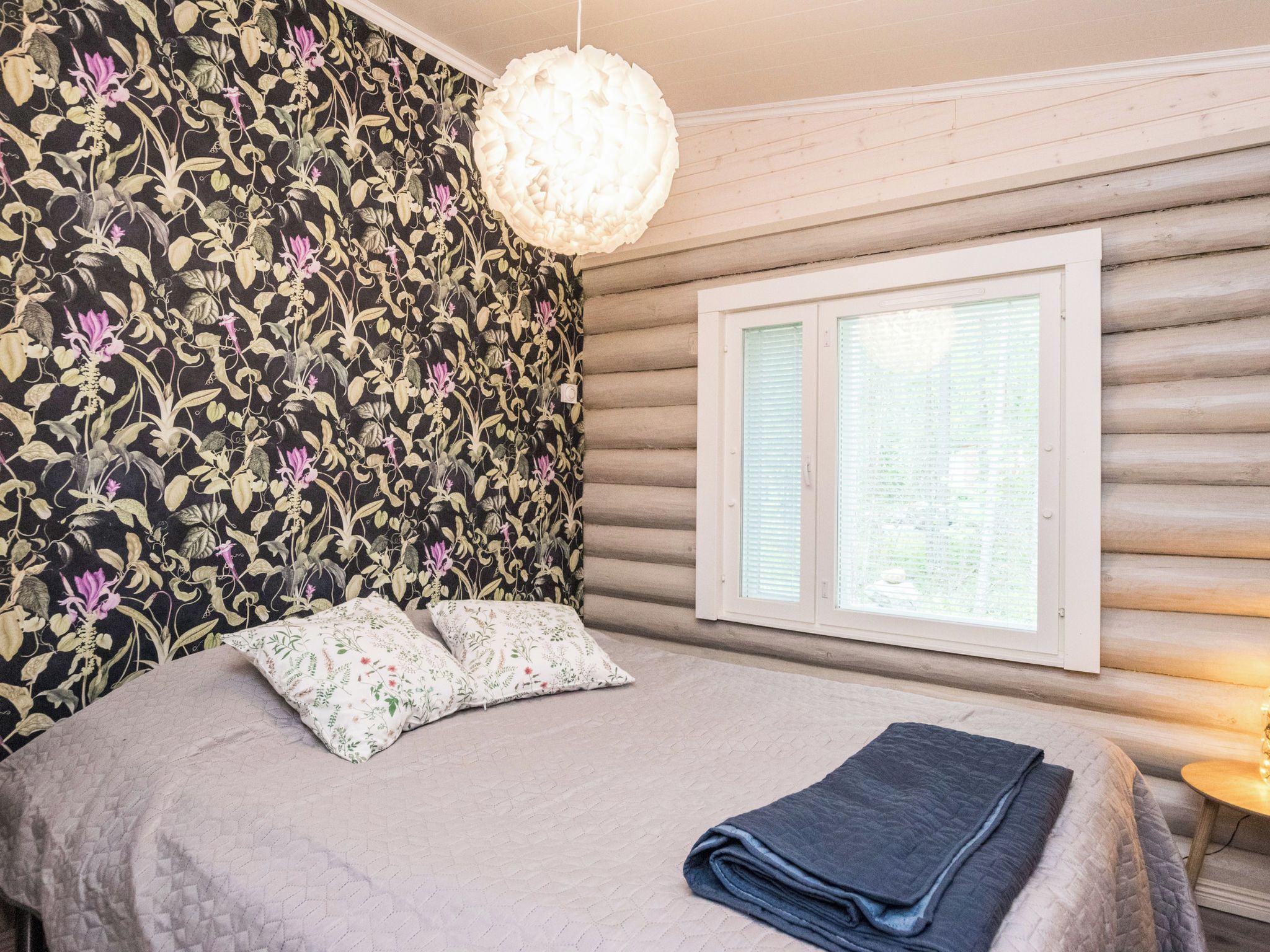 A bedroom with a bed, two pillows, a hanging light fixture, and a window with blinds.