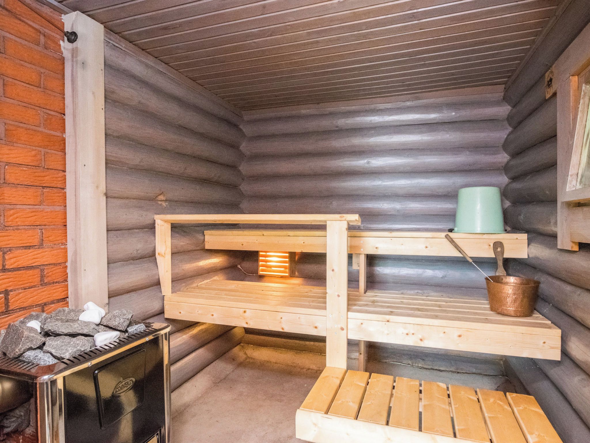 Una sauna con un banco de madera, una mesita y un calentador de metal.