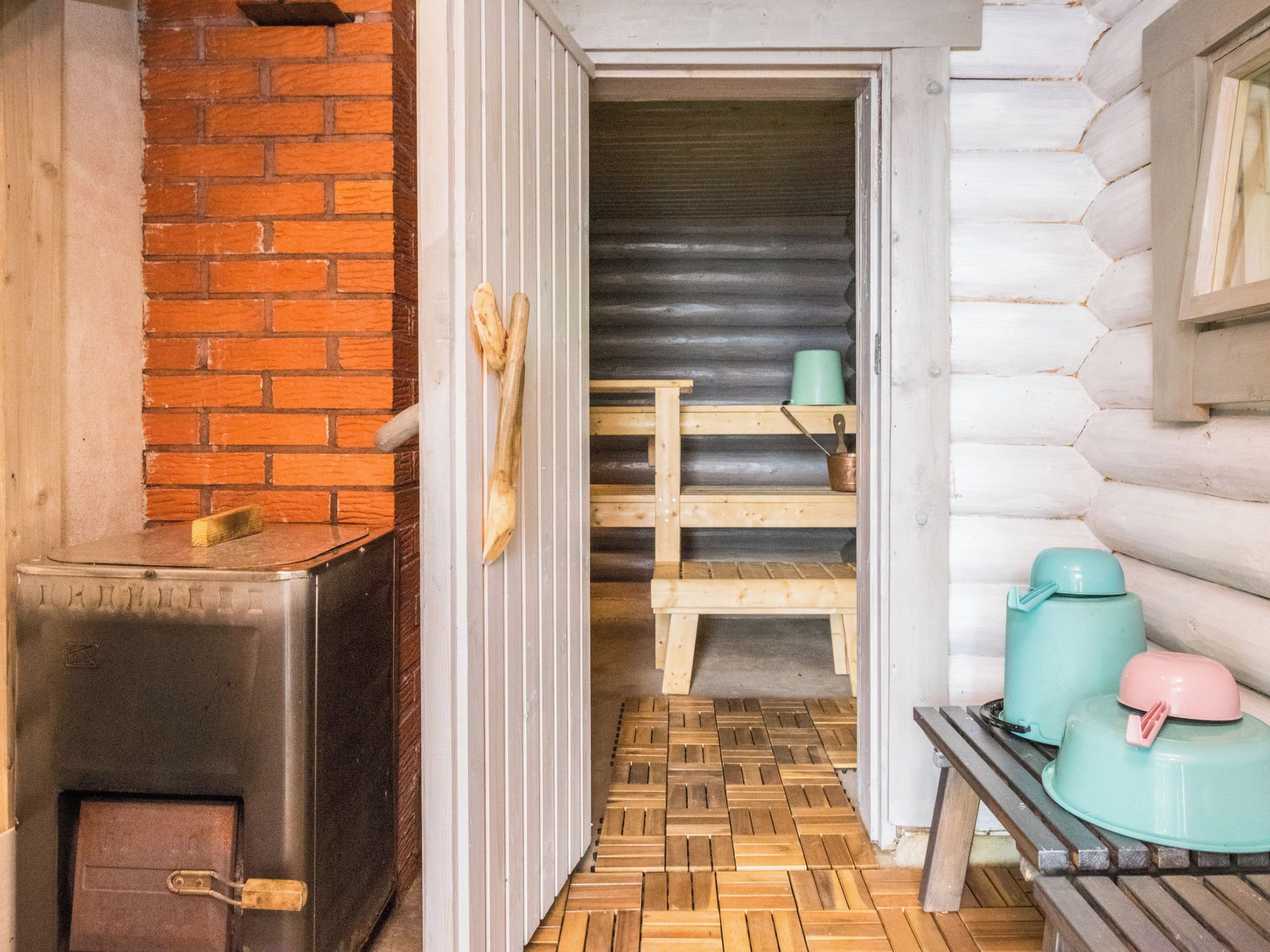 A rustic cabin interior with a wood-burning stove, a wooden bench, and a metal door.