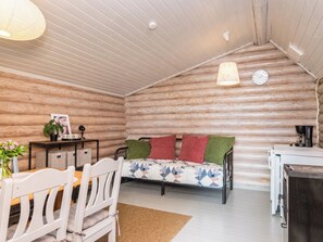 A cozy cabin interior with a wooden log wall, a bed with colorful bedding, a dining table with chairs, and a coffee machine. - Villa vehmas by Interhome (Sysmä)