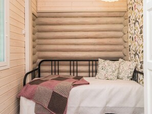 Ein Einzelbett mit einer Bettdecke und floralen Kissen in einem Blockhauszimmer.