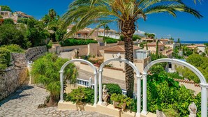 A coastal residential area with Mediterranean-style houses, a palm tree, and a stone pathway leading to a white archway. - Marques by Interhome (Dénia)