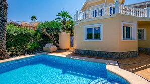A poolside view of a two-story house with a balcony, surrounded by lush greenery and a clear blue sky. - Marques by Interhome (Dénia)