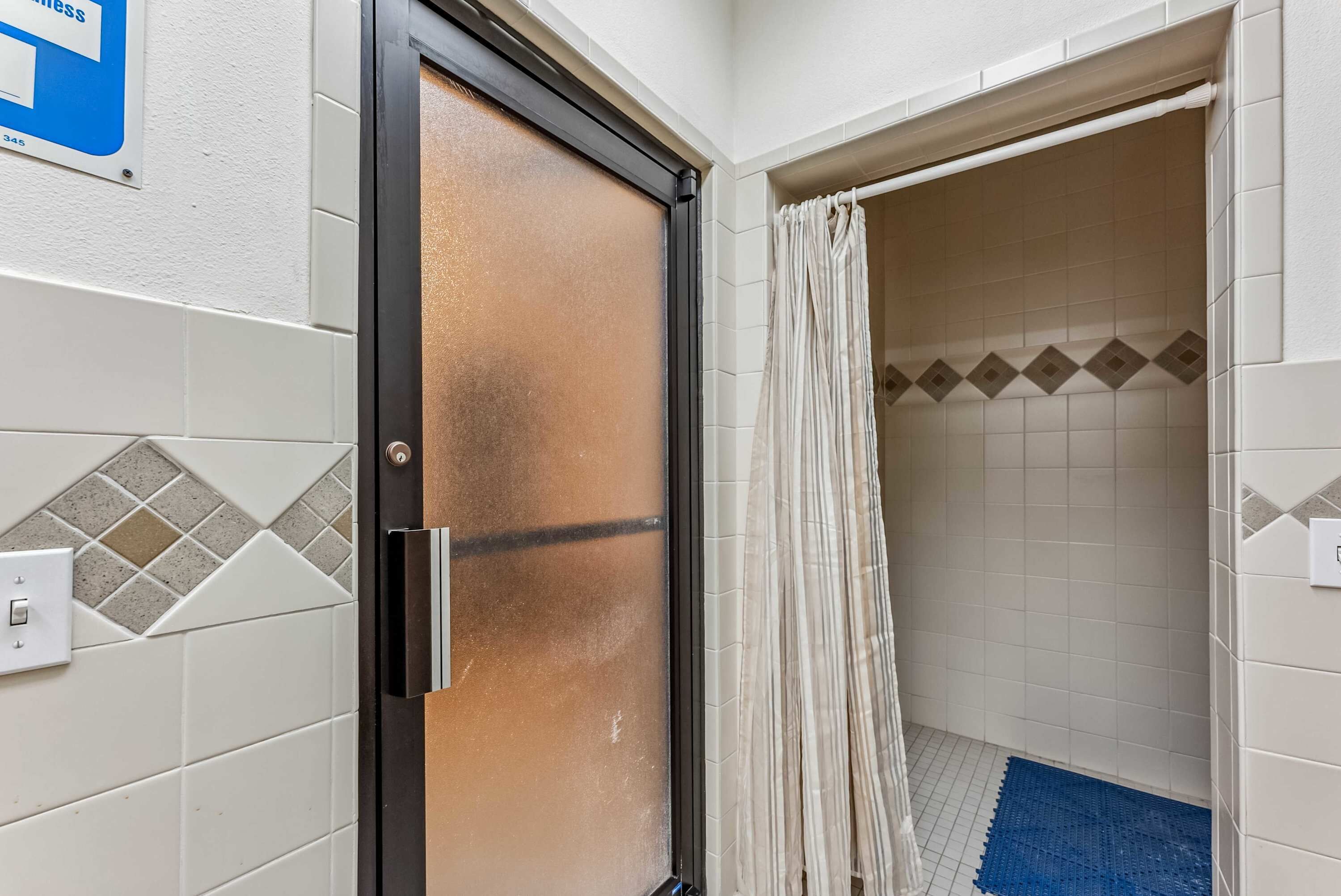A bathroom with a shower, tiled walls, a door with a frosted glass panel, and a blue mat on the floor.