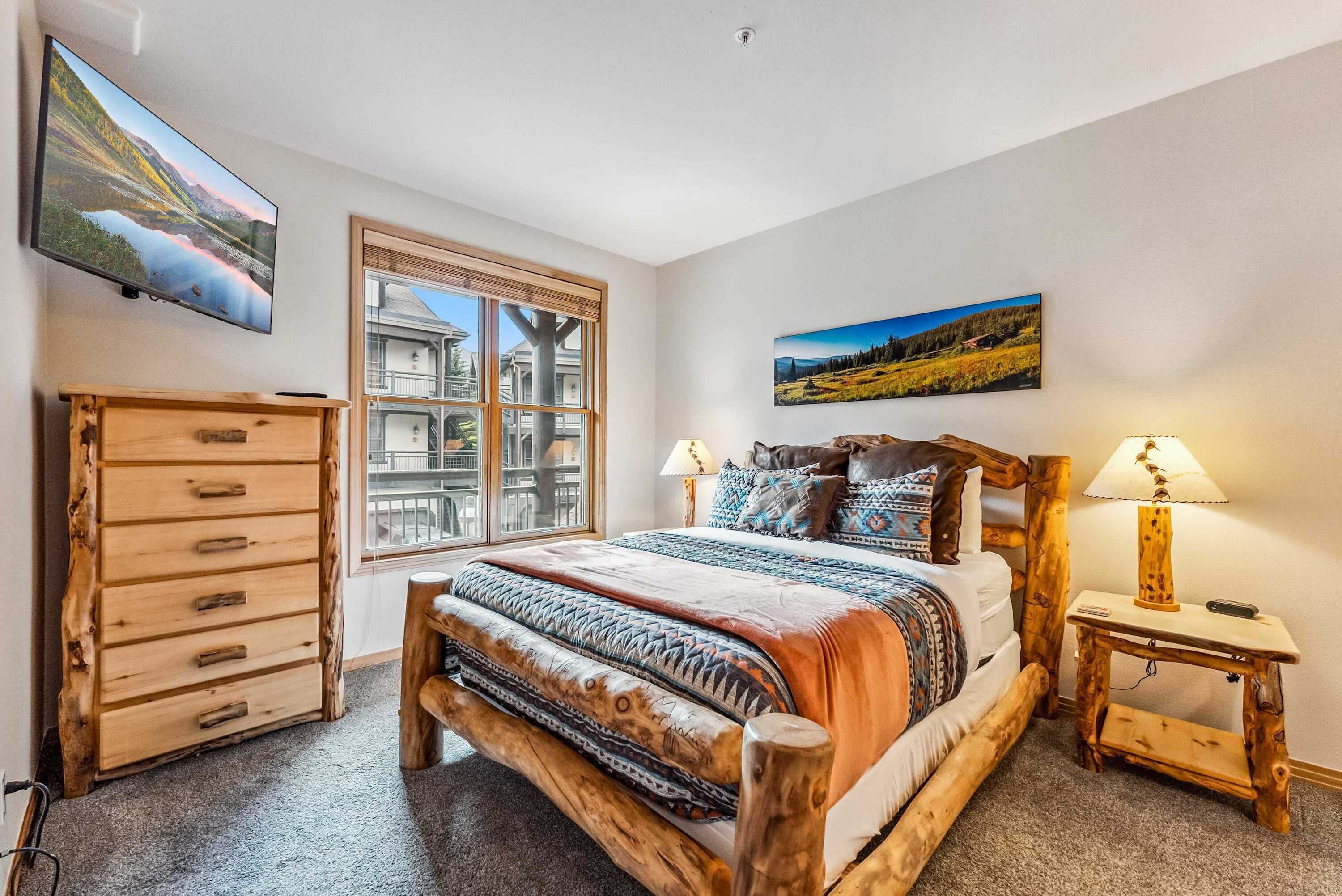 Une chambre à coucher avec un lit en bois, une commode, une fenêtre donnant sur une maison et deux lampes fixées au mur.