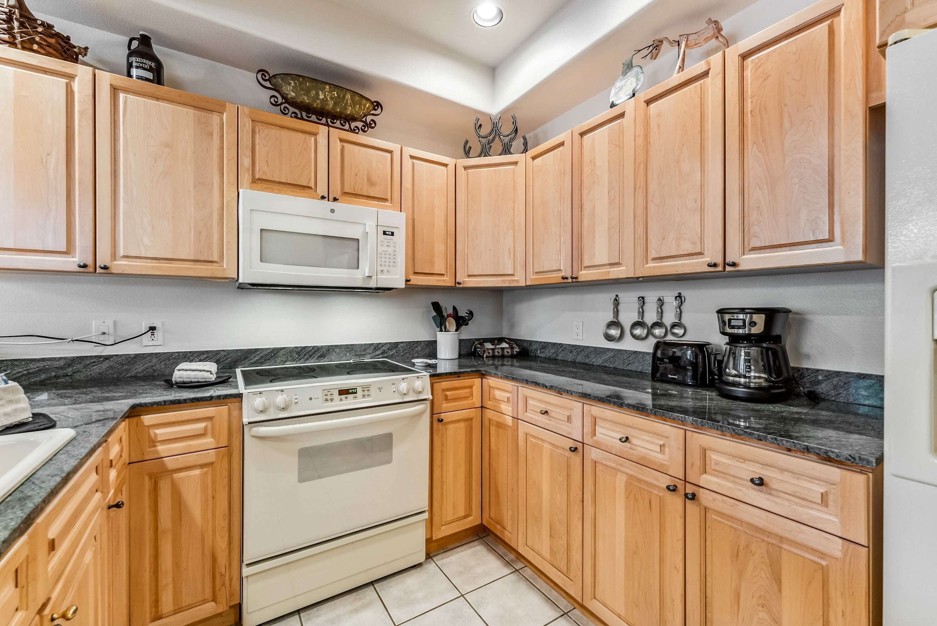A kitchen with wooden cabinets, a white microwave, a stove, and a coffee maker.