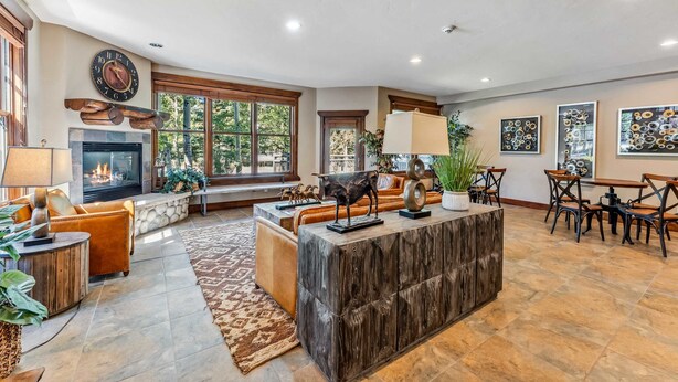 A spacious living room with a fireplace, a large clock, and a dining area with chairs and tables. - Breckenridge Condo with Hot Tub Access (Breckenridge)