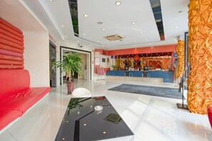 A hotel lobby with a reception desk, seating area, and a large potted plant.
