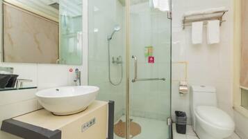 Un baño con ducha envuelta en vidrio, un lavamanos blanco, un inodoro y un perchero para toallas.