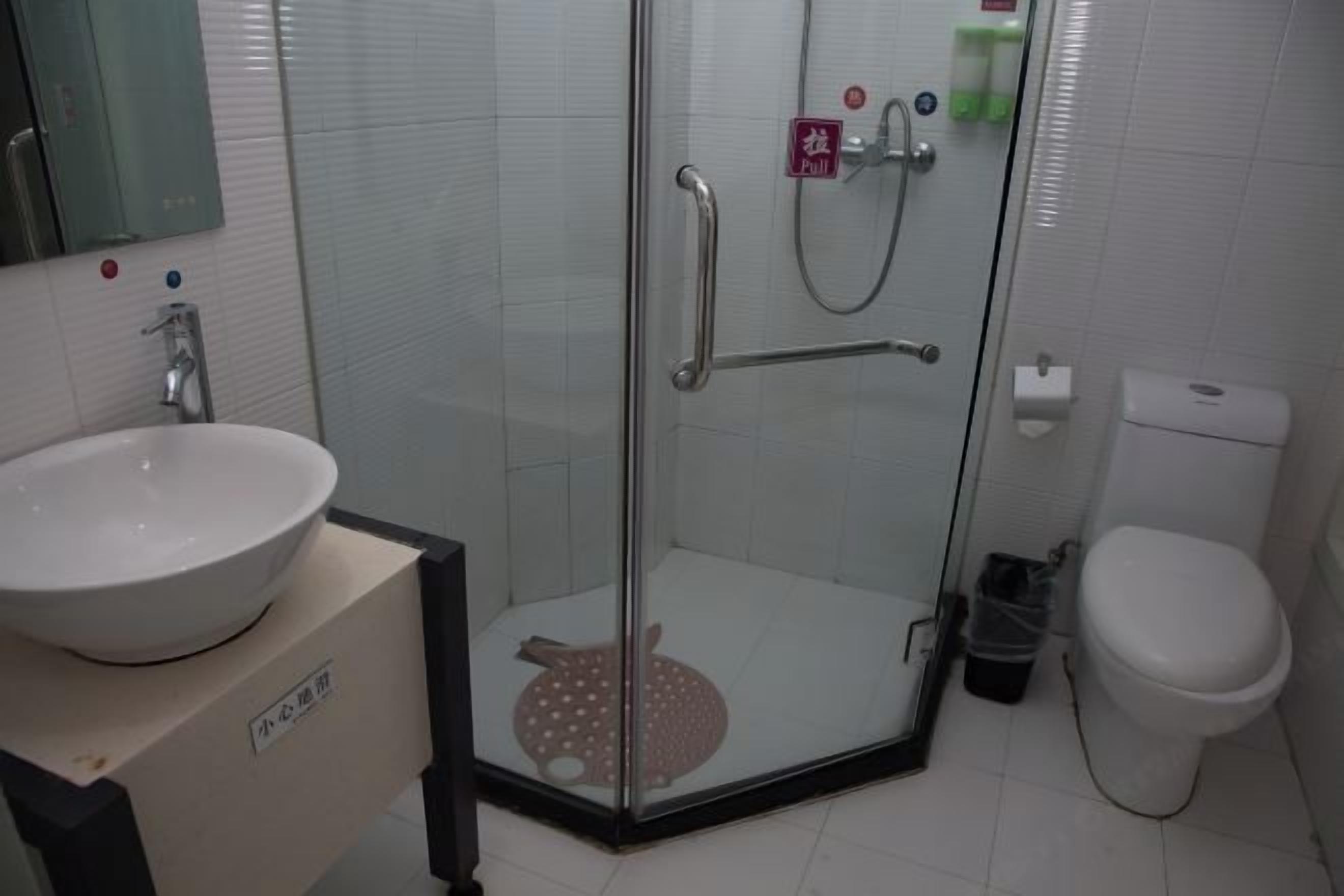 Un baño con ducha compartimentada con vidrio, un lavamanos blanco y un inodoro.