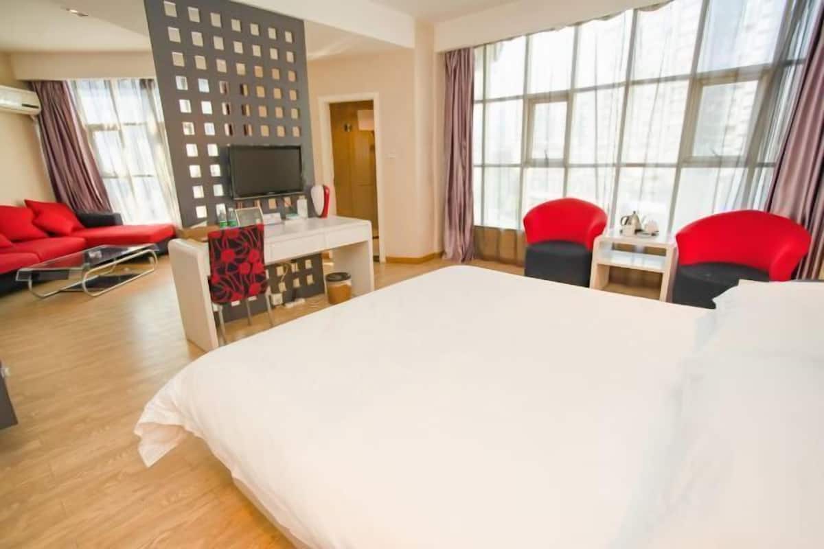A hotel room with a large bed, a desk with a chair, a TV, and a seating area with two chairs.