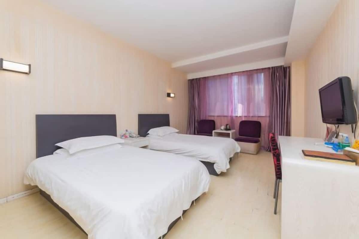 A hotel room with two beds, a desk with a TV, a small table, and a window with curtains.