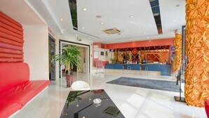 A hotel lobby with a reception desk, a red seating area, a black coffee table, and a large potted plant. - Fuerte Hotel Leqing Haian (Yueqing)