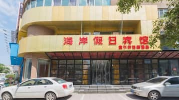 A hotel with a yellow facade and a red sign. There are two cars parked in front.