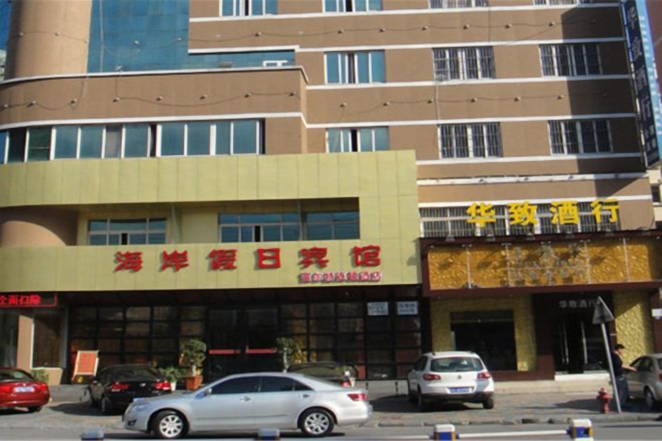 Un edificio con un letrero que dice '海滨休闲旅馆', indicando un hotel o resort. Hay coches estacionados adelante y el edificio tiene varios pisos con ventanas.