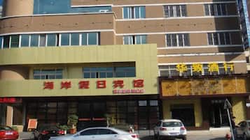 Un edificio con un letrero que dice '海滨休闲旅馆', indicando un hotel o resort. Hay coches estacionados adelante y el edificio tiene varios pisos con ventanas.
