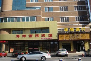 A building with a sign that reads '海滨休闲旅馆' indicating a hotel or resort. There are cars parked in front, and the building has multiple floors with windows. - Fuerte Hotel Leqing Haian (Yueqing)