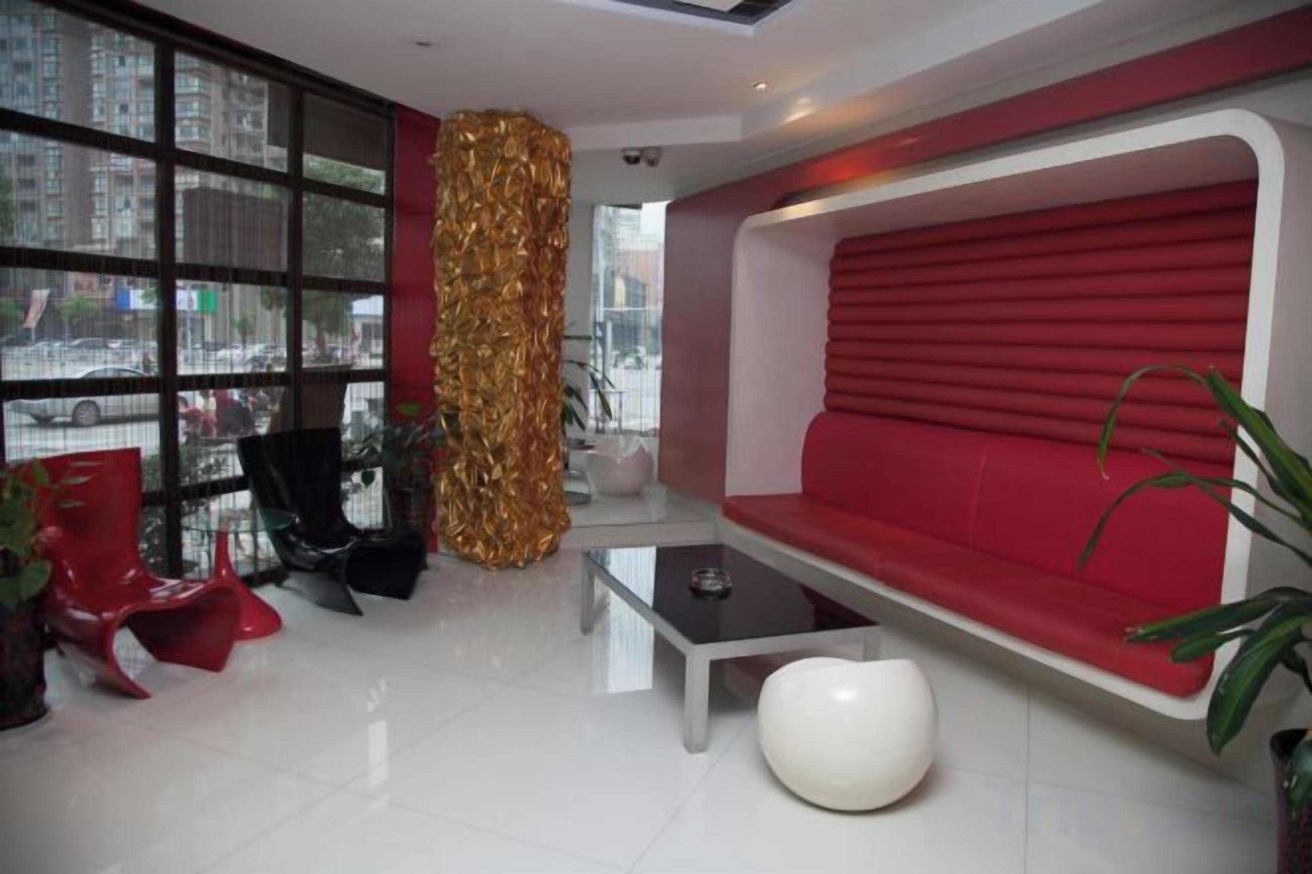 Un interior moderno con un sofá rojo, sillas negras, una mesa de centro de vidrio y un ventanal grande.