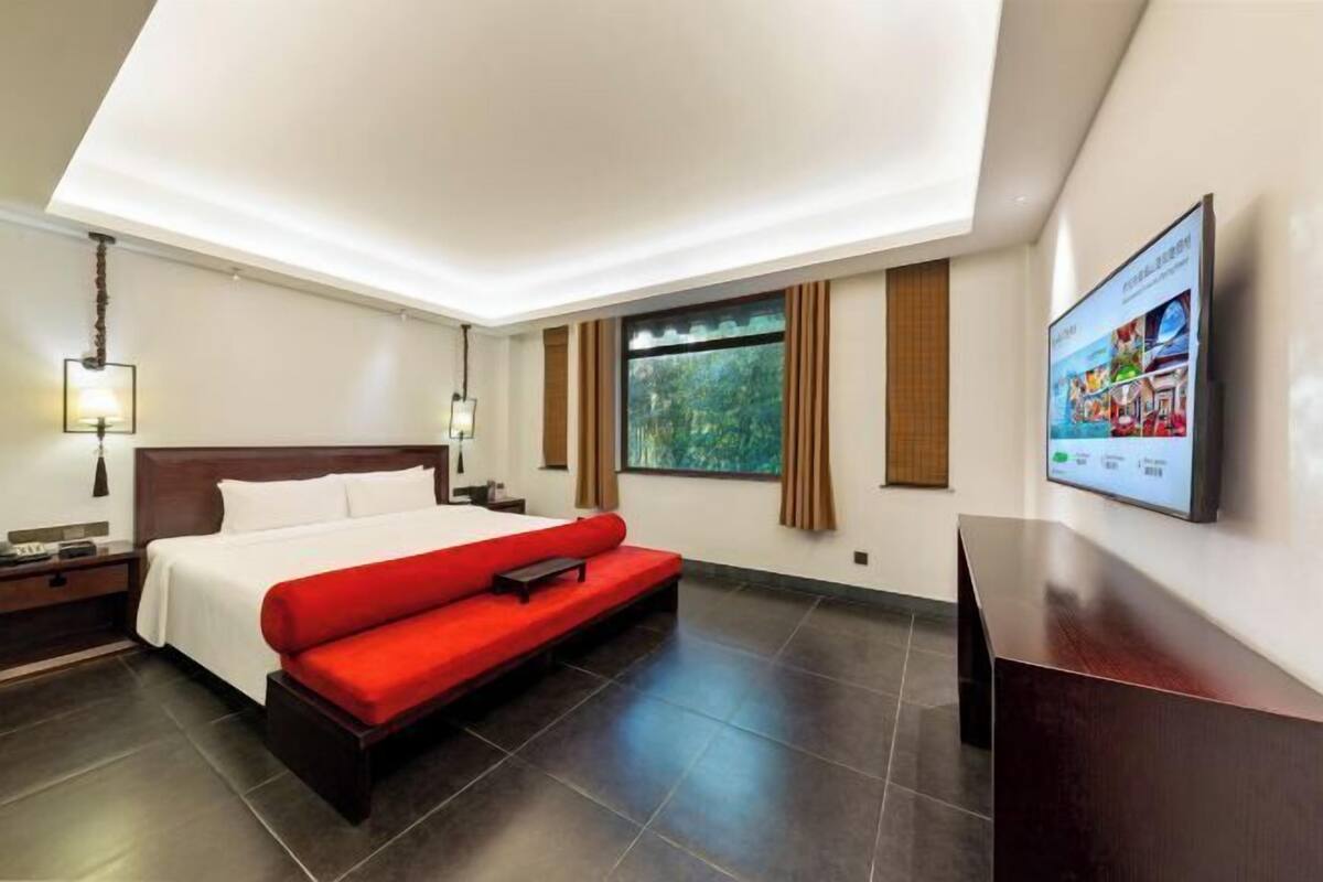 A modern hotel room with a large bed, a desk, and a television on the wall.