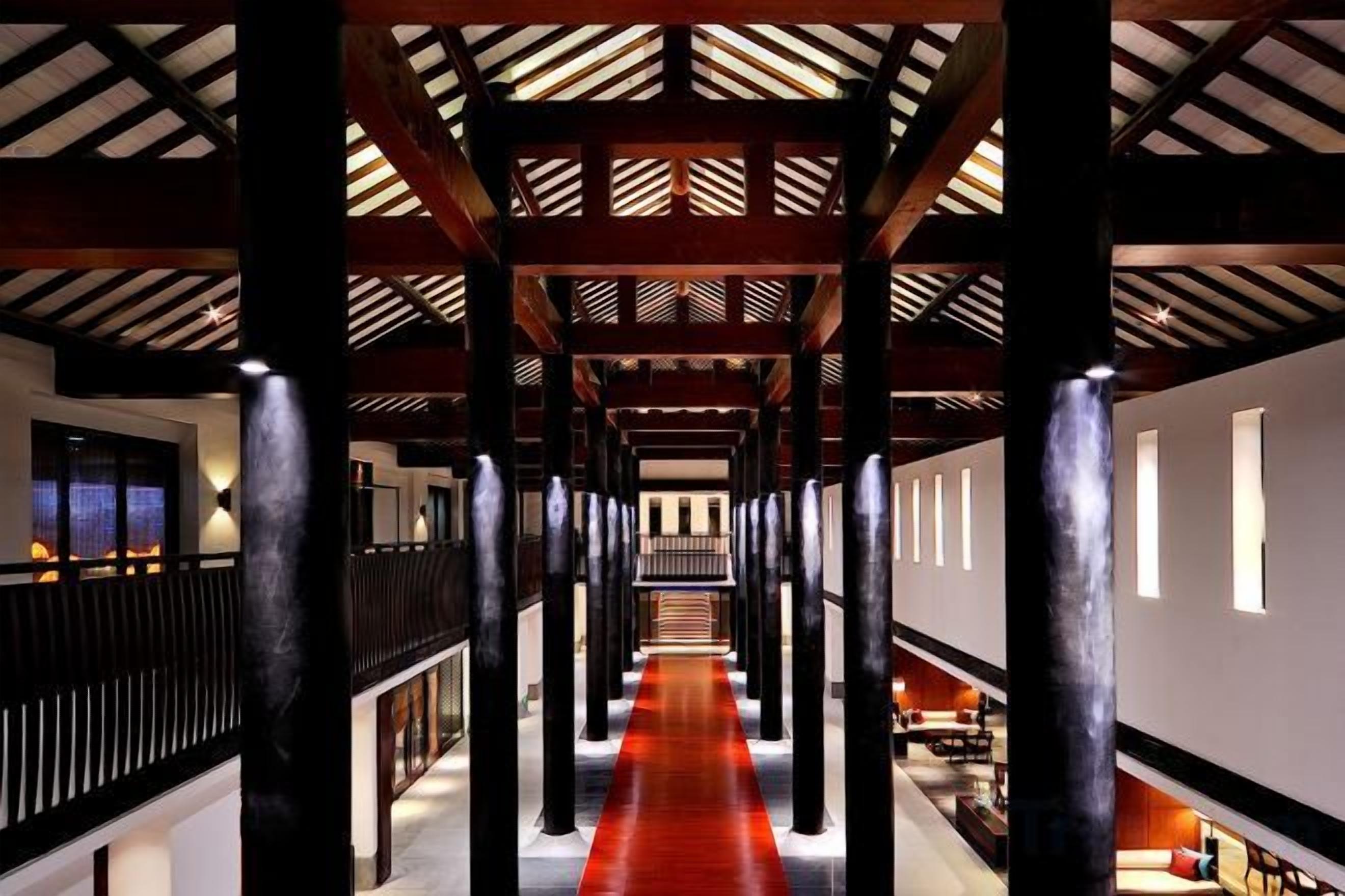 A corridor with a red carpet, wooden beams, and columns.