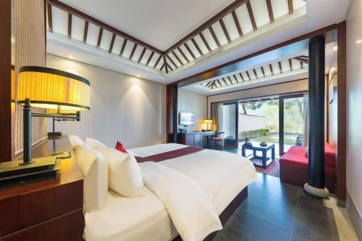 A hotel room with a large bed, a desk, a chair, and a view of the outdoors.
