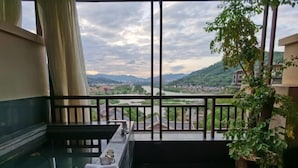 Un balcón con vistas a un río y montañas, un banco y una planta en maceta.