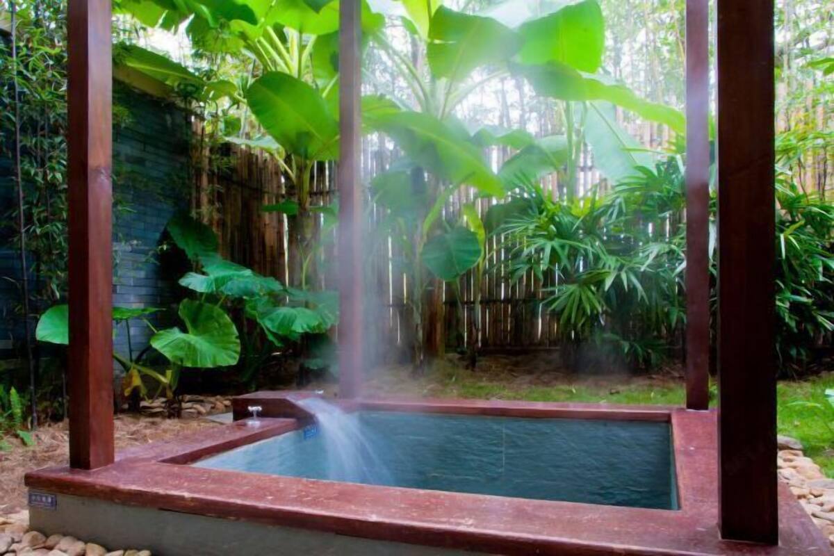 A hot spring with a wooden frame, surrounded by lush greenery and a bamboo fence.