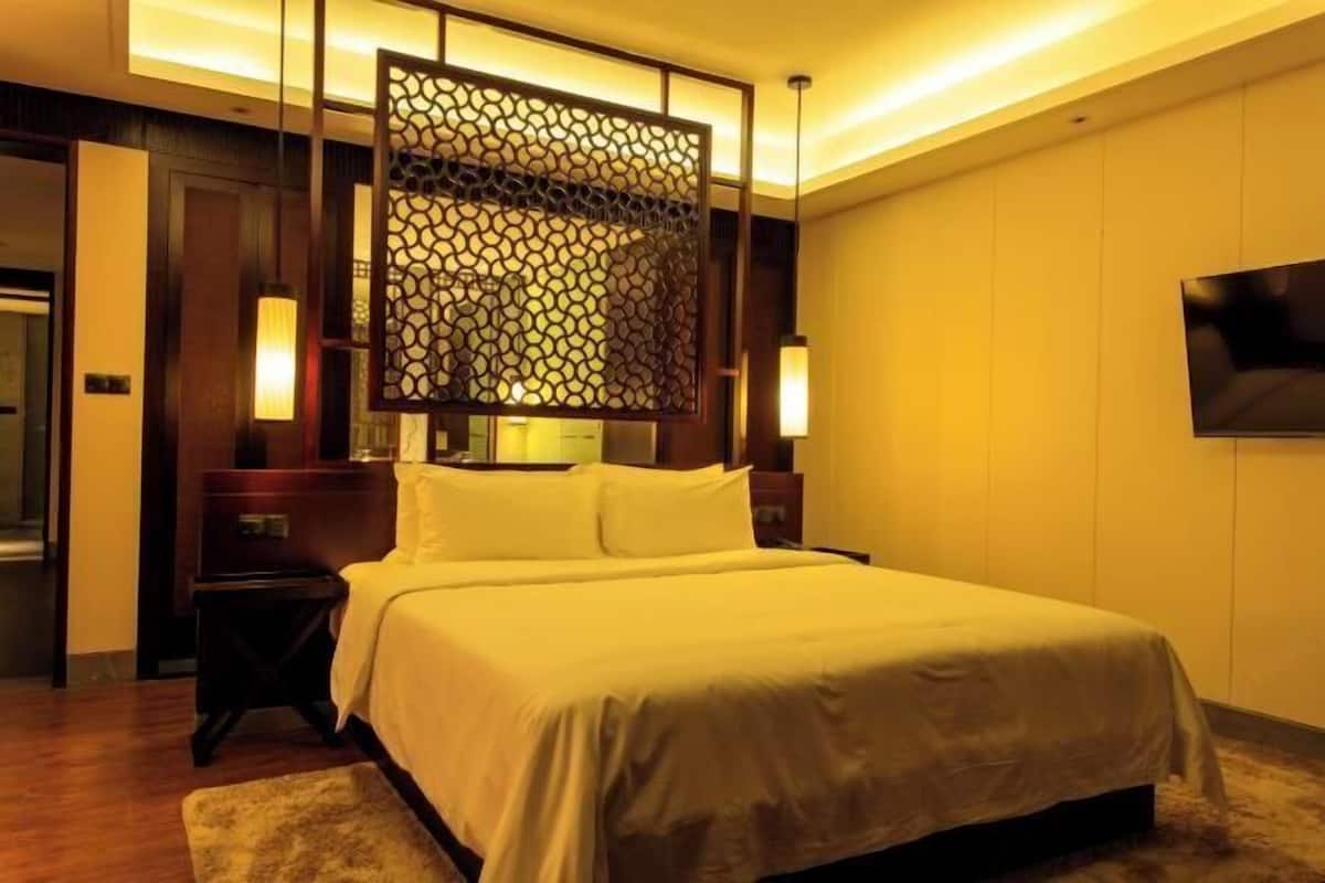 A hotel room with a large bed, a decorative screen, two bedside lamps, and a TV on the wall.