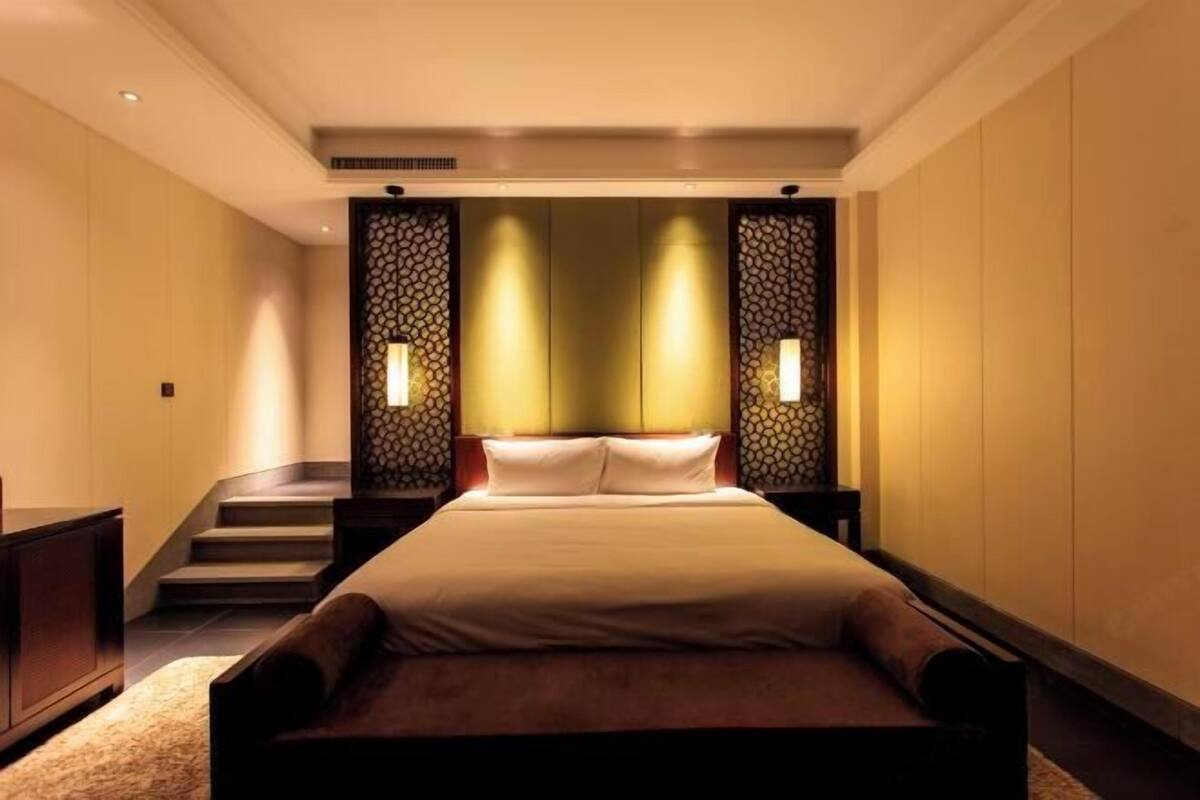 A hotel room with a large bed, a small sofa, a staircase, and a decorative wall panel.