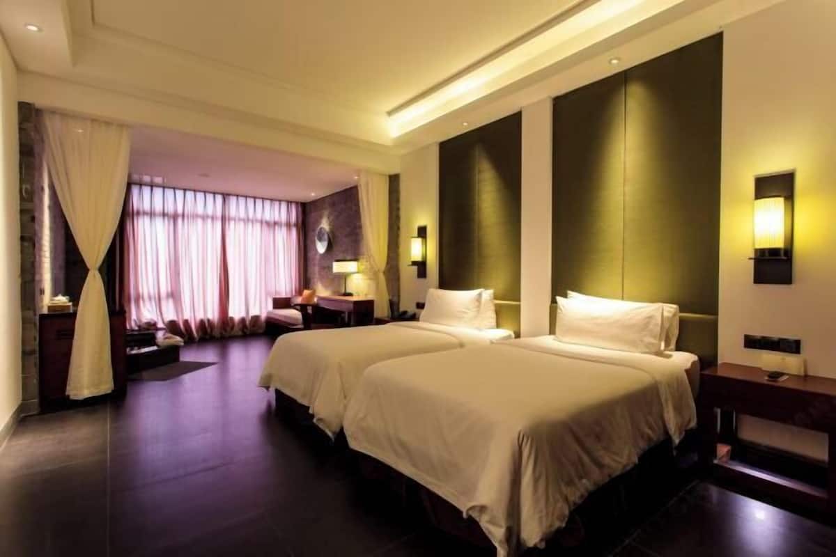 A hotel room with two beds, a desk, a chair, and a large window with curtains.